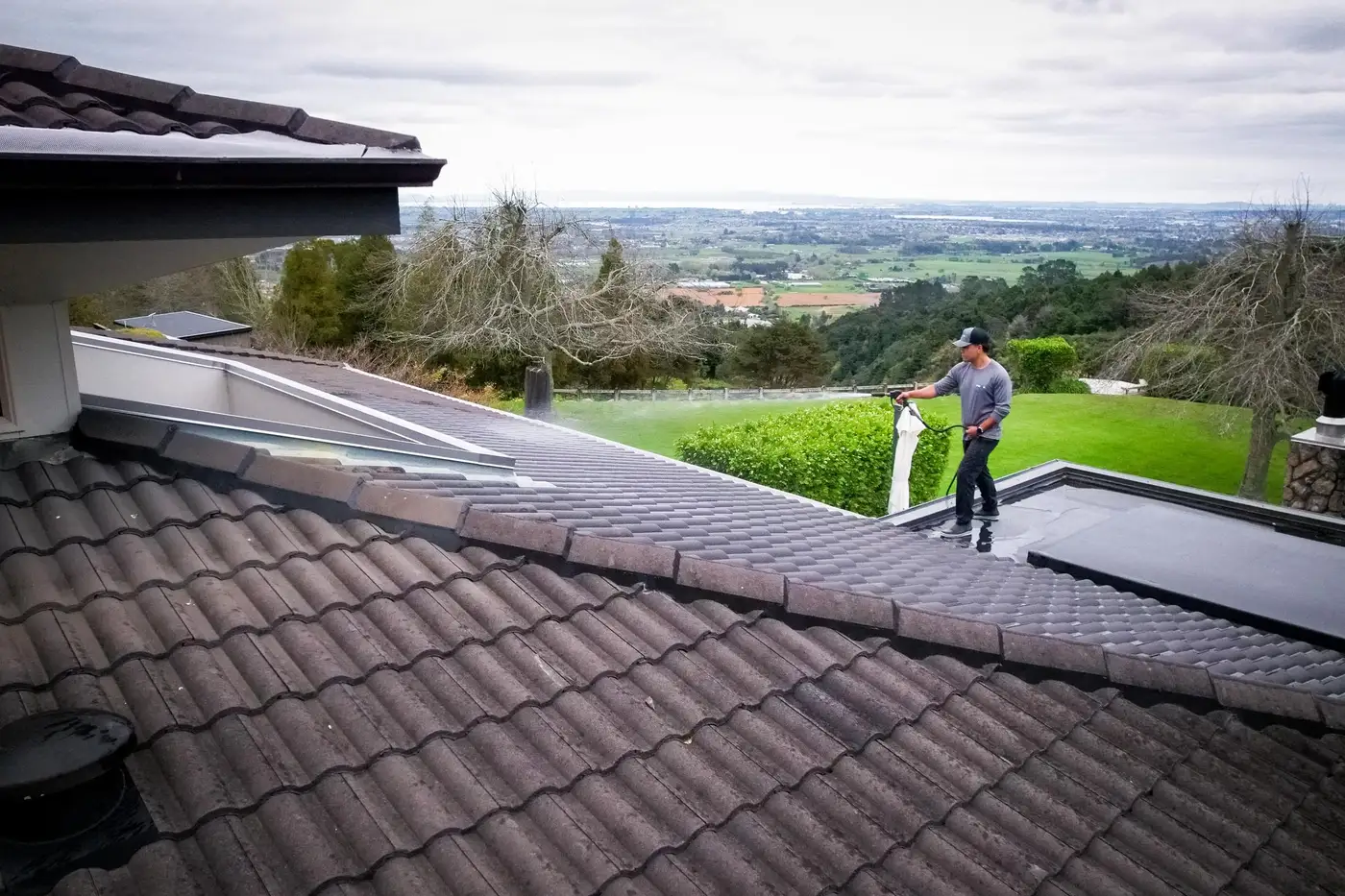 Logan on a concrete tile roof with the hose, a wide valley view behind him